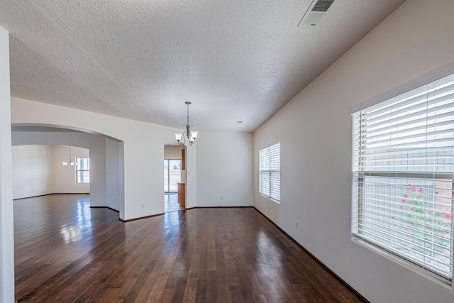 empty room with visible vents, a notable chandelier, dark wood-type flooring, a textured ceiling, and arched walkways