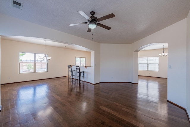 empty room featuring visible vents, ceiling fan with notable chandelier, wood finished floors, arched walkways, and a textured ceiling