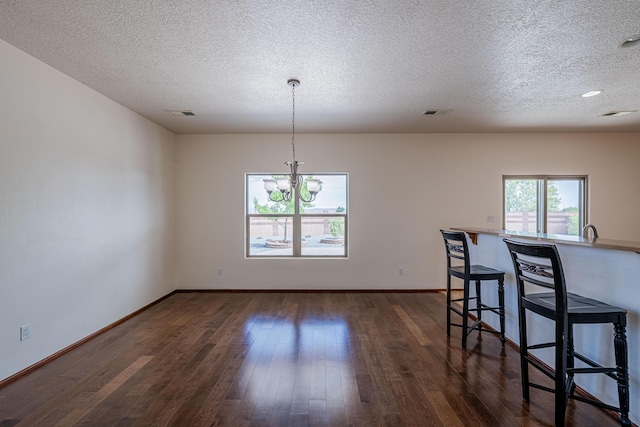 unfurnished dining area featuring visible vents, a notable chandelier, a textured ceiling, dark wood finished floors, and baseboards