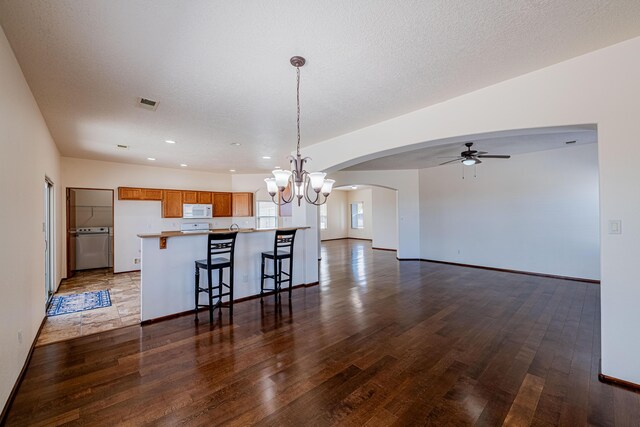 kitchen featuring white microwave, ceiling fan with notable chandelier, brown cabinetry, and dark wood-type flooring