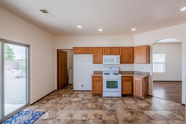 kitchen featuring visible vents, light countertops, brown cabinets, arched walkways, and white appliances