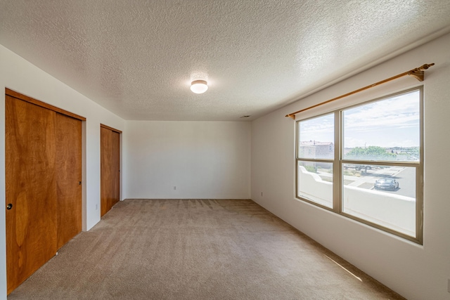 unfurnished bedroom with light colored carpet, two closets, and a textured ceiling