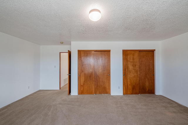 unfurnished bedroom with visible vents, carpet, multiple closets, and a textured ceiling