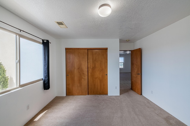 unfurnished bedroom with carpet flooring, visible vents, a closet, and a textured ceiling