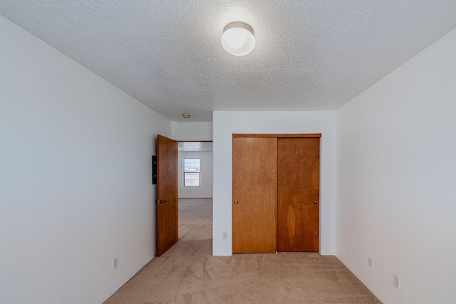 unfurnished bedroom with light carpet, a textured ceiling, and a closet