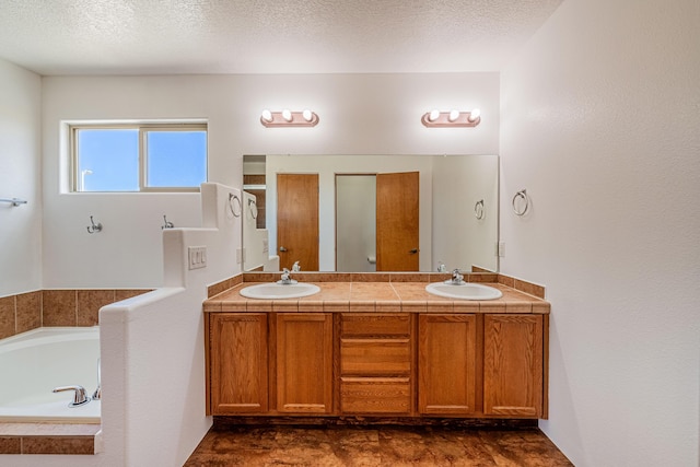 full bath with a sink, a textured ceiling, a bath, and double vanity