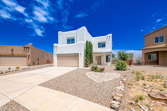 pueblo-style home with stucco siding, an attached garage, concrete driveway, and fence