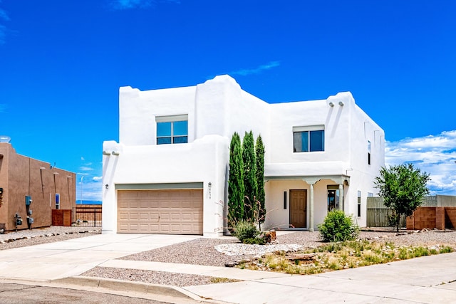 pueblo-style home featuring concrete driveway, fence, a garage, and stucco siding