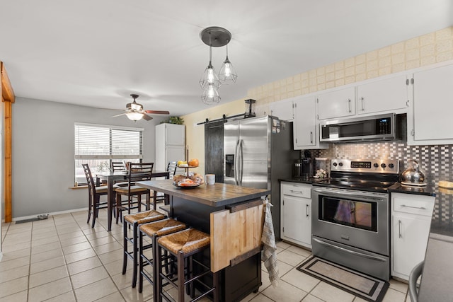 kitchen with a ceiling fan, backsplash, stainless steel appliances, a barn door, and light tile patterned floors