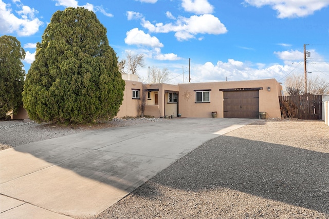 pueblo-style home with stucco siding, a garage, driveway, and fence