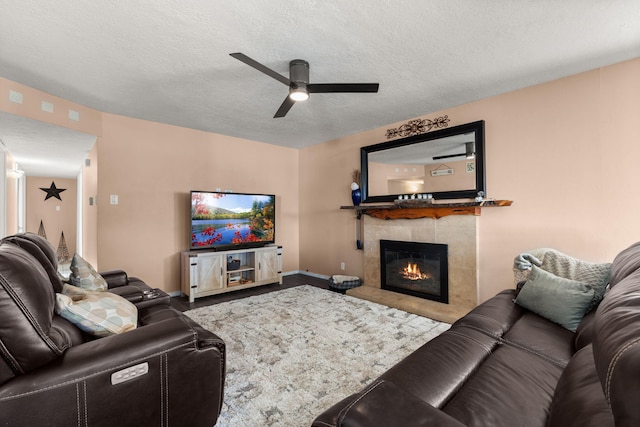 living area featuring a tiled fireplace, a ceiling fan, baseboards, and a textured ceiling