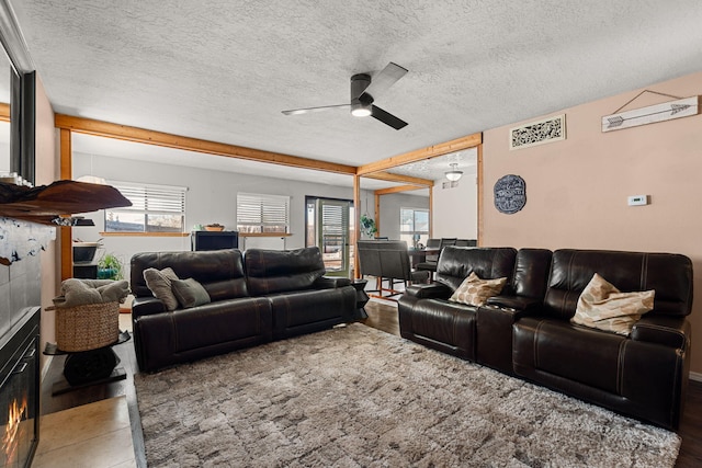 living room featuring a glass covered fireplace, wood finished floors, a textured ceiling, and ceiling fan