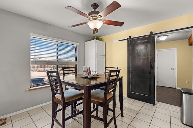 dining space featuring light tile patterned floors, a barn door, baseboards, and ceiling fan