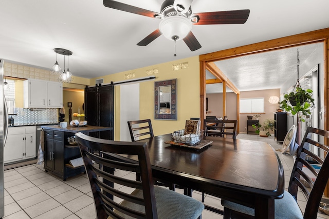 dining space with light tile patterned floors, ceiling fan, and a barn door