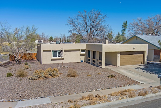 pueblo-style house with concrete driveway, fence, a garage, and stucco siding