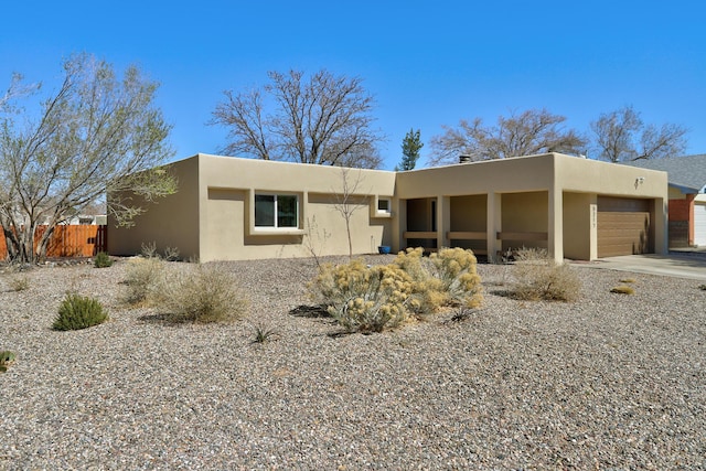 pueblo-style house with stucco siding, a garage, and fence