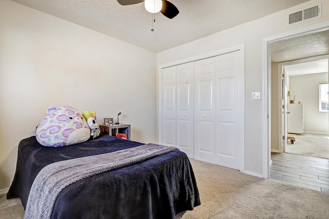 carpeted bedroom with baseboards, visible vents, ceiling fan, a closet, and a textured ceiling