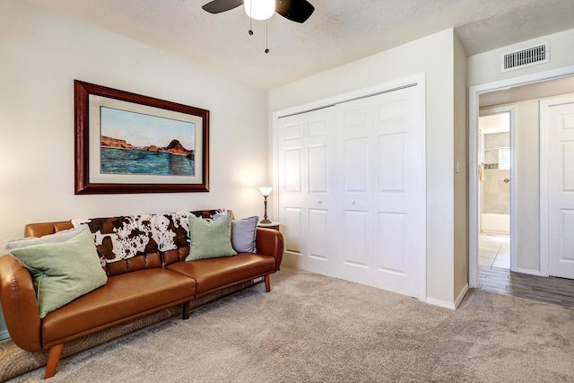 carpeted living room featuring visible vents, a textured ceiling, and ceiling fan