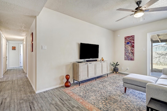 living room with ceiling fan, wood finished floors, baseboards, and a textured ceiling