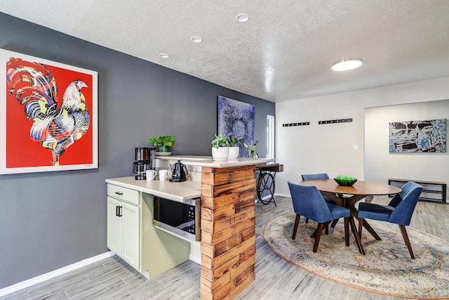 dining area with a textured ceiling, light wood-type flooring, and baseboards