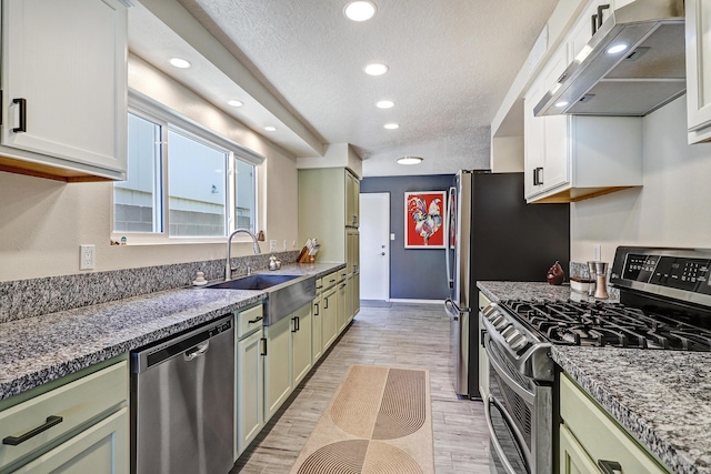 kitchen featuring a sink, appliances with stainless steel finishes, light wood-style floors, exhaust hood, and green cabinetry