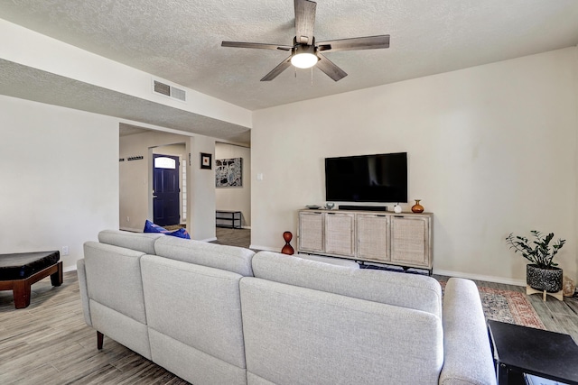 living room featuring visible vents, a textured ceiling, a ceiling fan, and light wood-style floors