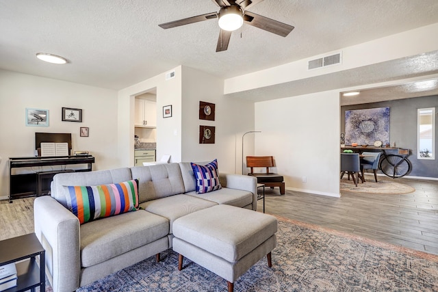 living room featuring visible vents, a textured ceiling, baseboards, and wood finished floors