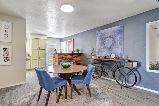 dining room with light wood finished floors, a textured ceiling, and baseboards