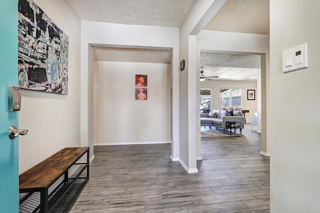 hall with baseboards, a textured ceiling, and wood finished floors