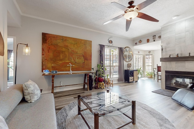 living room with ceiling fan, ornamental molding, a tile fireplace, wood finished floors, and a textured ceiling