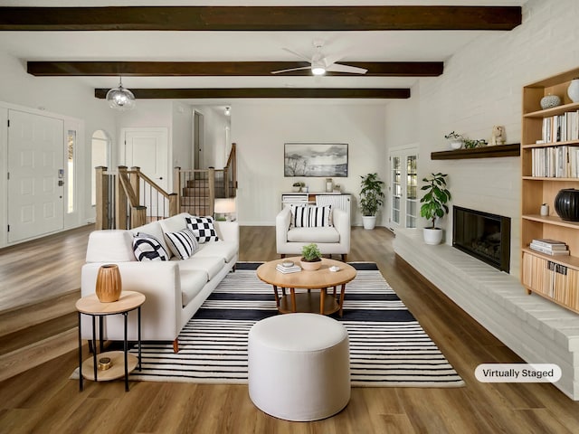 living area with ceiling fan, stairway, a brick fireplace, and wood finished floors