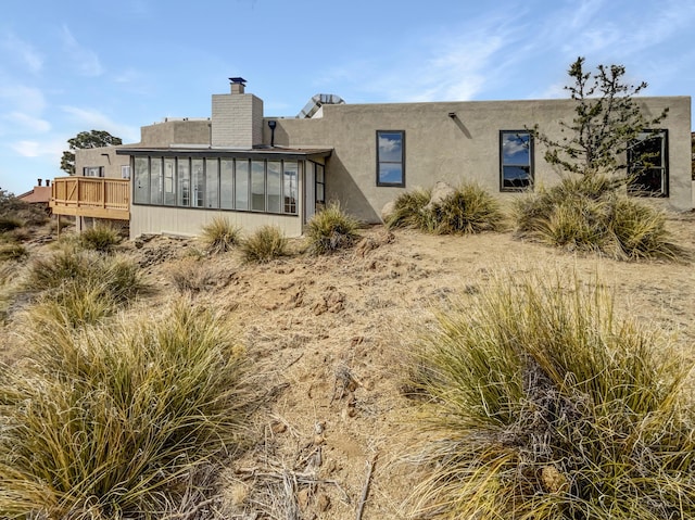 rear view of house with stucco siding, a chimney, and a sunroom