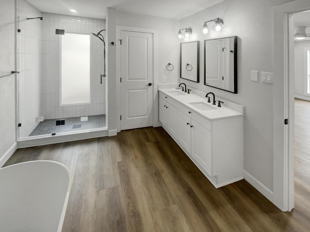 bathroom with wood finished floors, baseboards, a tile shower, and a sink