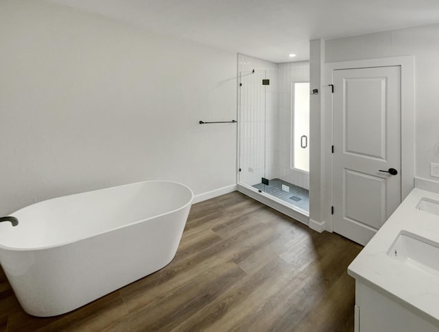 bathroom with wood finished floors, baseboards, double vanity, a stall shower, and a freestanding bath