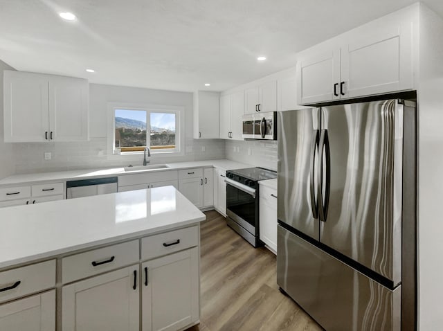 kitchen featuring a sink, tasteful backsplash, stainless steel appliances, light wood-style floors, and white cabinets