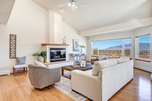 living room featuring baseboards, high vaulted ceiling, wood-type flooring, a glass covered fireplace, and a mountain view