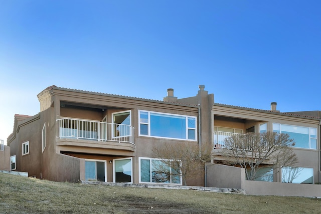 rear view of house with a balcony and stucco siding