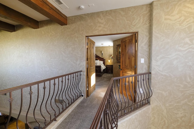 hall featuring visible vents, wallpapered walls, beamed ceiling, carpet floors, and an upstairs landing