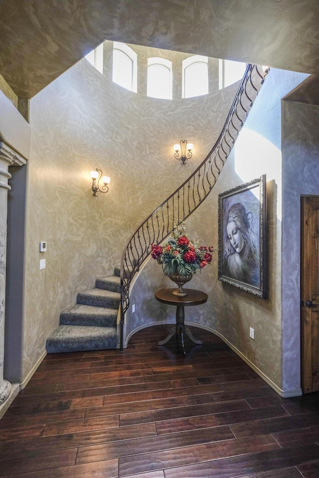 stairs with plenty of natural light, a high ceiling, and wood finished floors