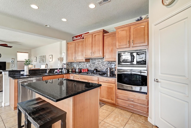kitchen with a sink, appliances with stainless steel finishes, a peninsula, light tile patterned flooring, and decorative backsplash