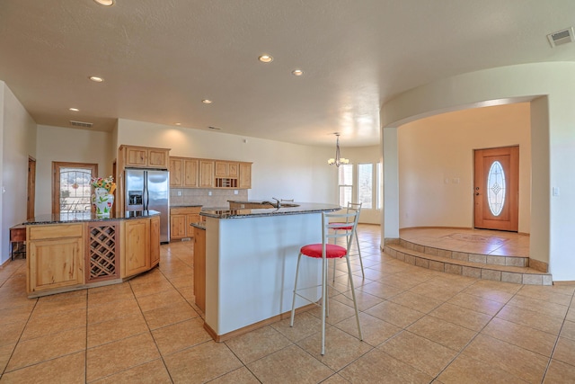 kitchen with light tile patterned floors, a center island with sink, visible vents, stainless steel fridge, and backsplash