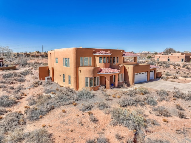 southwest-style home with concrete driveway, a tiled roof, an attached garage, and stucco siding