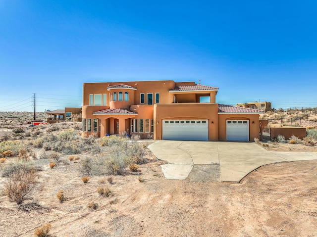 pueblo-style house featuring stucco siding, a tiled roof, concrete driveway, and an attached garage