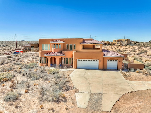 pueblo revival-style home featuring stucco siding, driveway, and a tiled roof