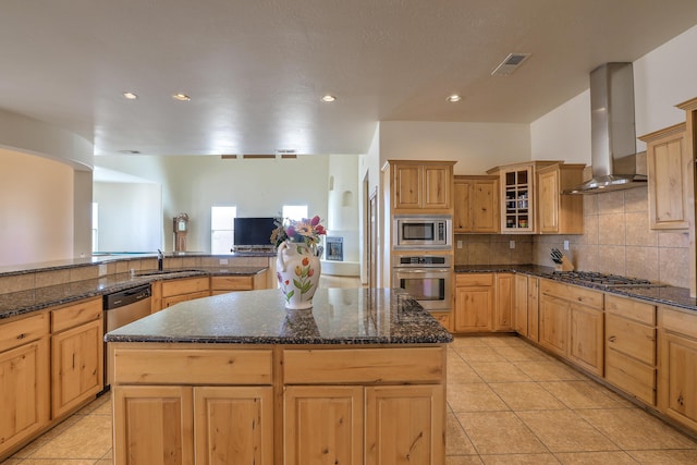 kitchen featuring visible vents, a sink, appliances with stainless steel finishes, wall chimney range hood, and backsplash