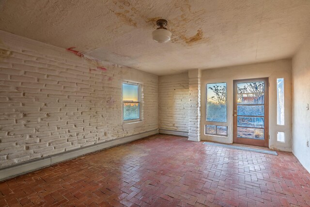 3805 Riverview Rd NW, Albuquerque, NM 87105 - spare room with a textured ceiling, brick floors, and brick wall