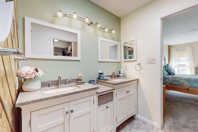 bathroom with double vanity, connected bathroom, baseboards, and a sink