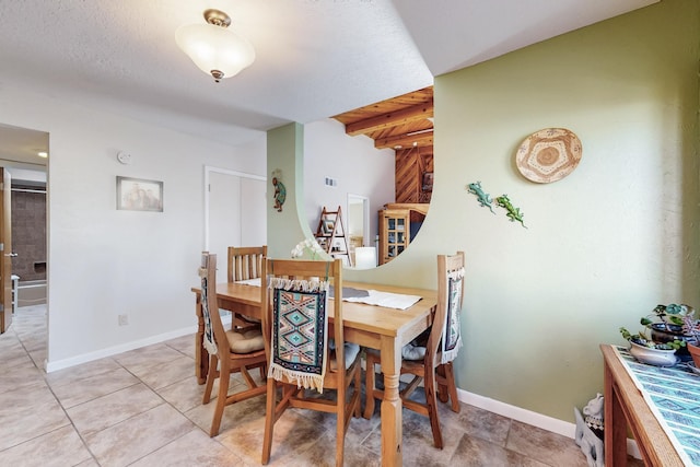 dining space featuring light tile patterned floors, beamed ceiling, and baseboards