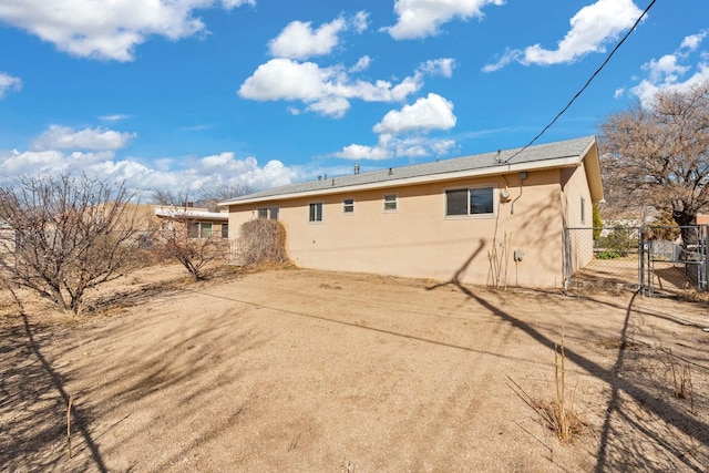 rear view of property with a gate, stucco siding, and fence