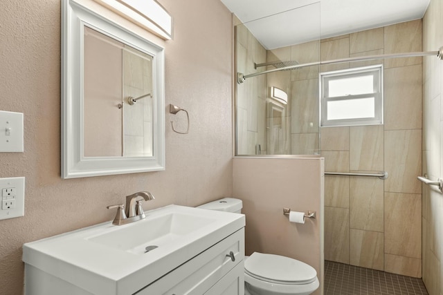 bathroom featuring a textured wall, toilet, vanity, and a tile shower